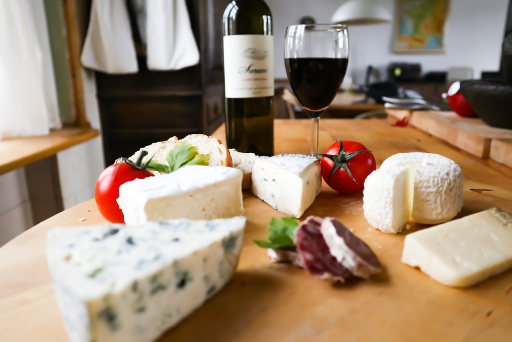 A Wooden Surface Featuring a Glass and Bottle of Red Wine, Two Tomatoes, Cured Meat, and Cheese