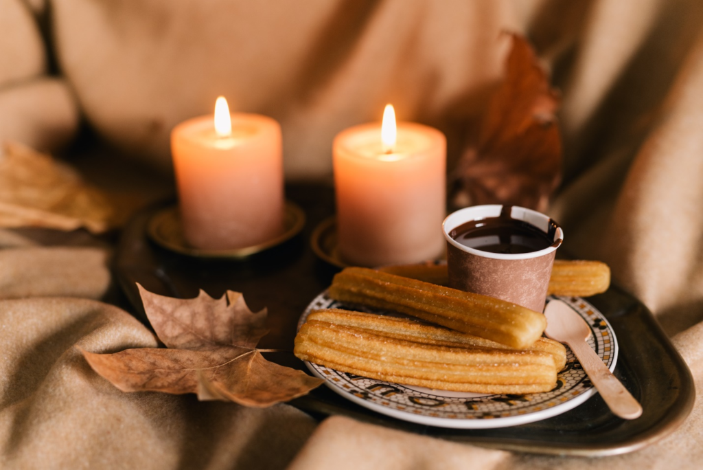 a plate of churros and chocolates next to candles