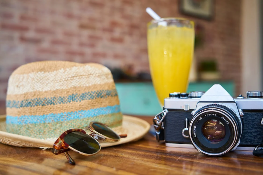 An image of a camera beside a hat and glasses on a table