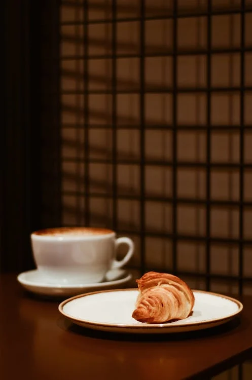 An image of bread on a plate next to a cup of coffee