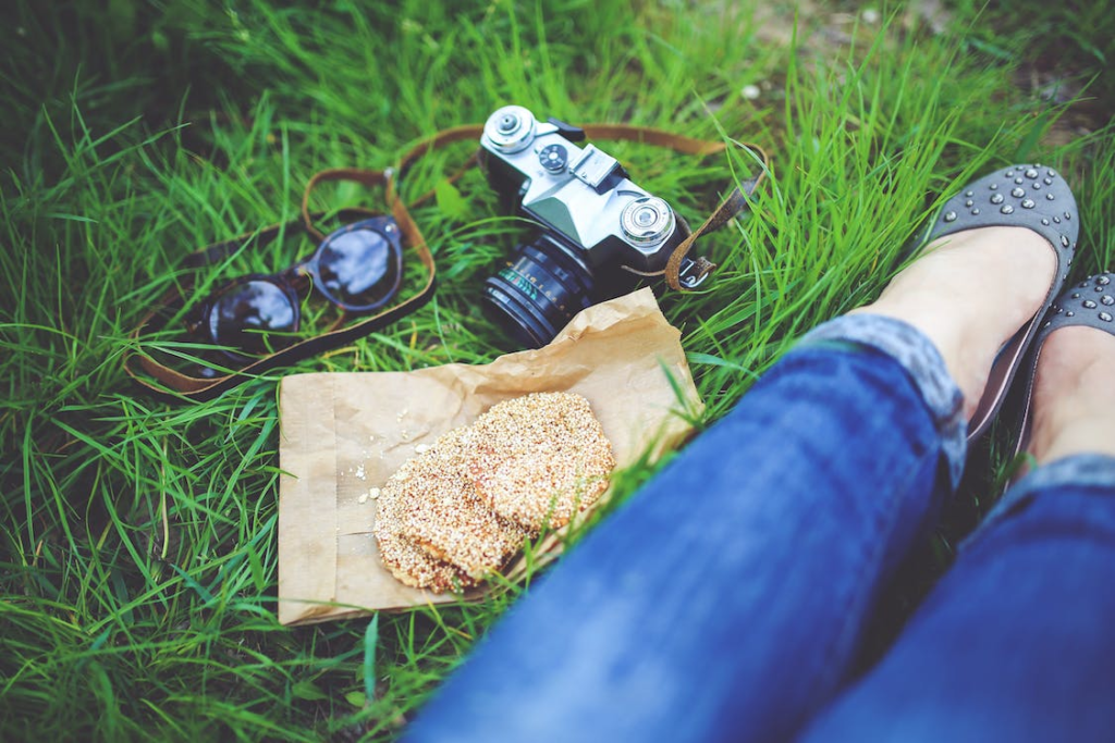 An image of a woman resting in the grass with cookies and a camera